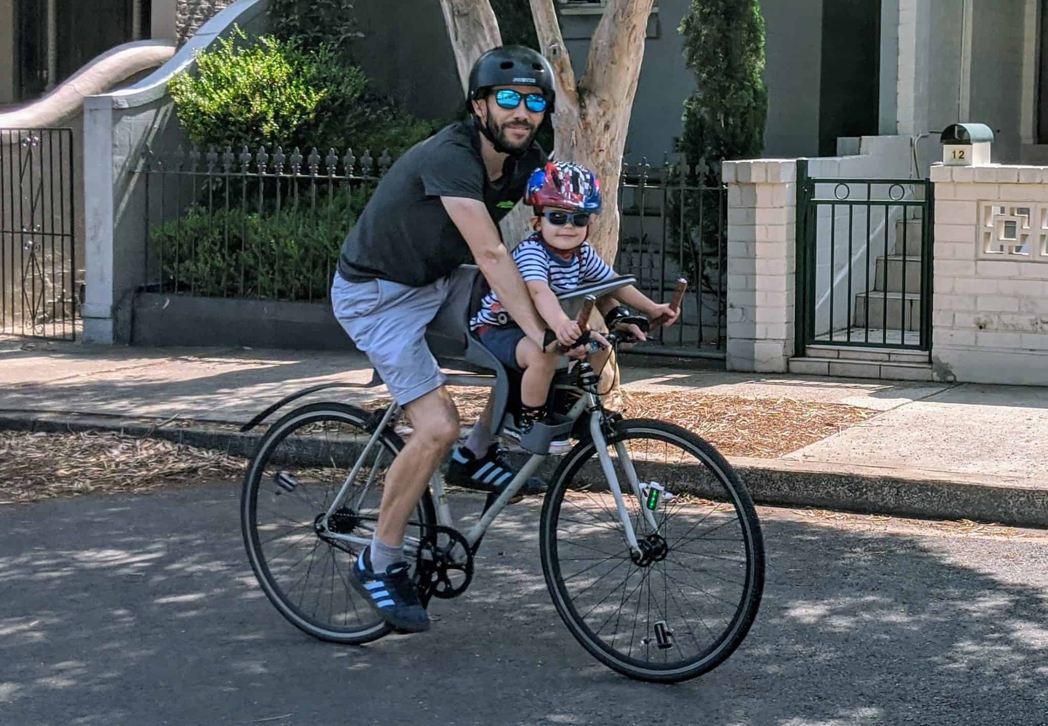 Parent and baby cycling together on a sunny street, baby in WeeRide centre-mounted bike seat
